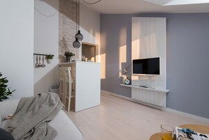 A modern living room with a white sofa, a dining area with a white table, and a mounted TV on a white panel.