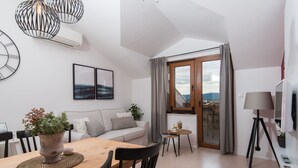 A modern living room with a wooden dining table, black chairs, a grey sofa, a potted plant, and a view through a glass door. - BonaMare apartments (Sveti Filip i Jakov)
