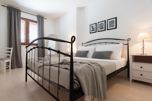 A bedroom with a bed, bedside table, lamp, and a chair.