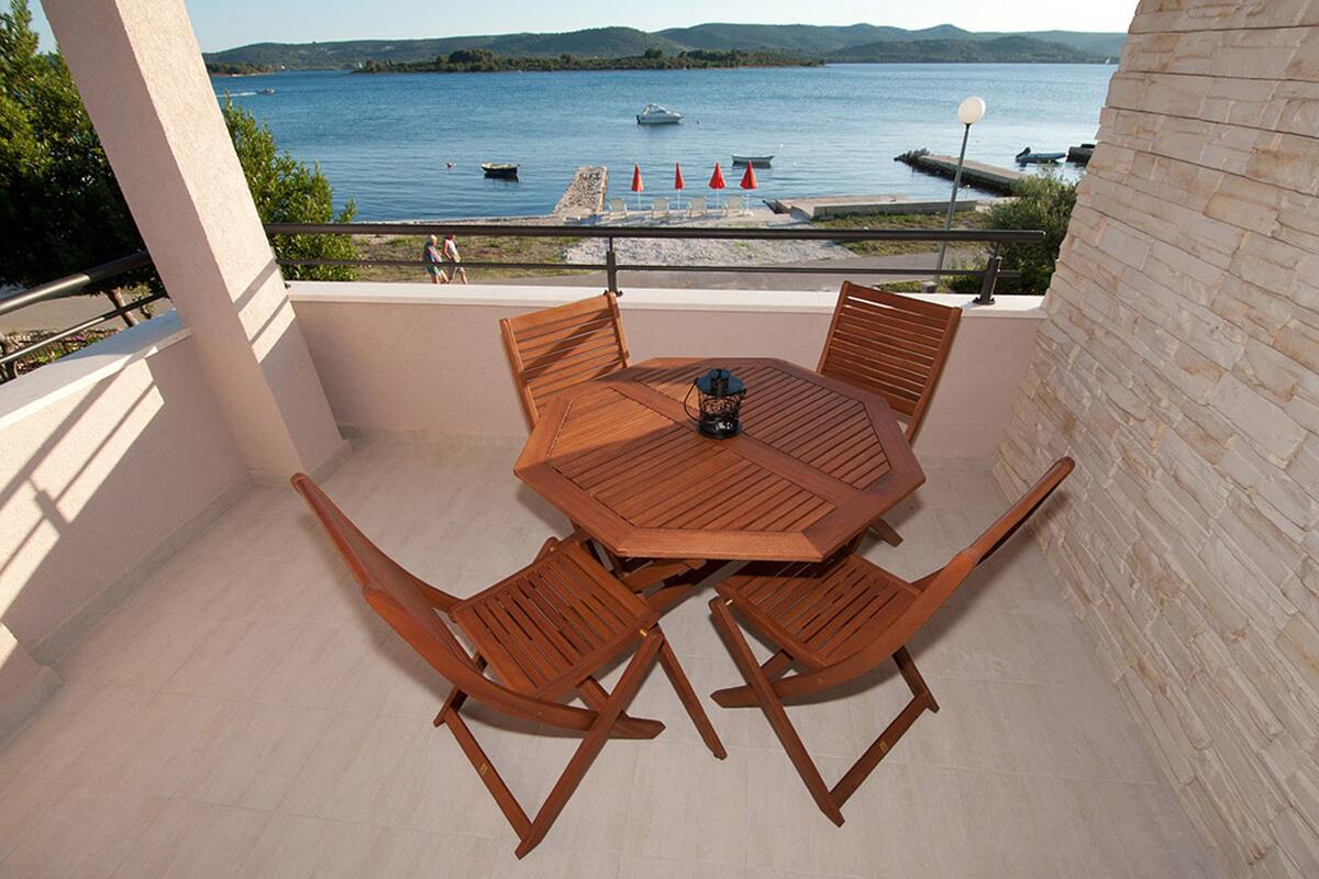 A balcony with a wooden table and chairs, overlooking a lake with boats and a dock.
