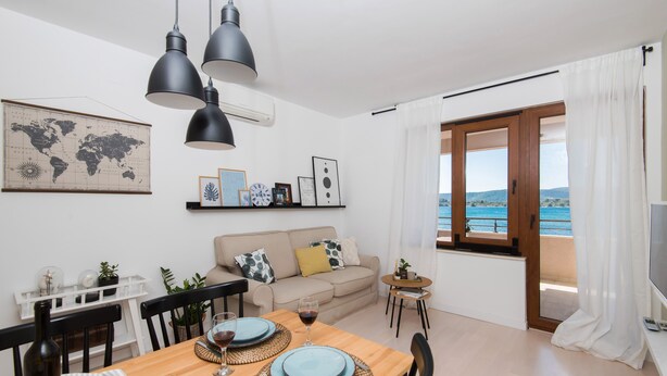 A dining area with a wooden table set for two, a world map on the wall, and a view of the sea through a large window. - BonaMare apartments (Sveti Filip i Jakov)