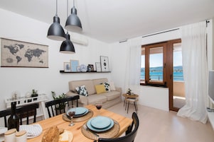 A dining area with a wooden table set for two, a world map on the wall, and a view of the sea through a large window.