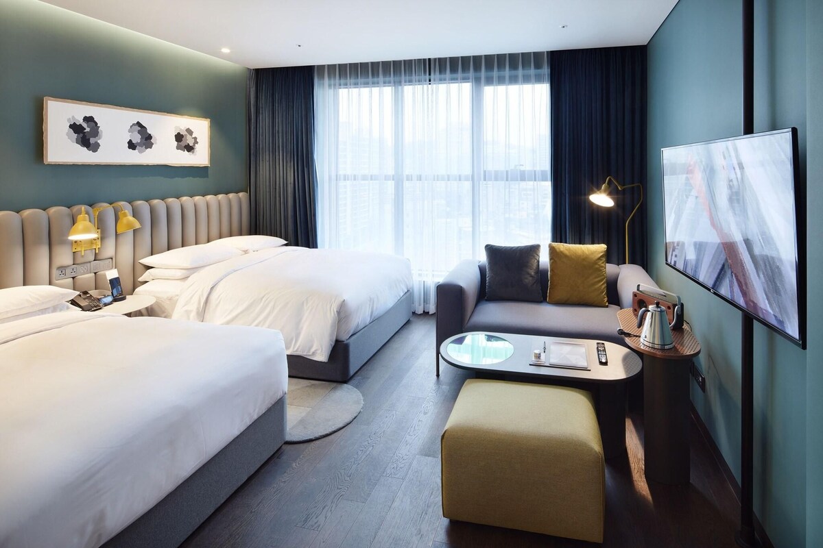 A hotel room with two beds, a sofa, a coffee table, and a TV.