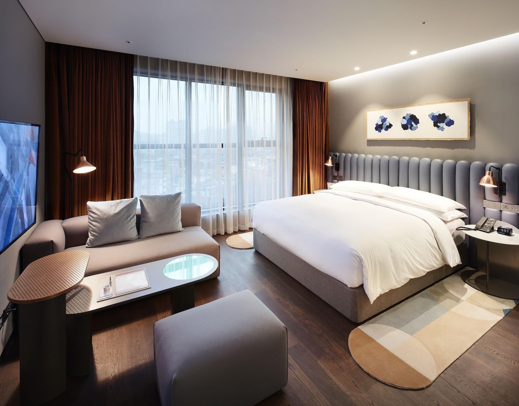 A modern hotel room with a large bed, a sofa, a small table, and a TV.