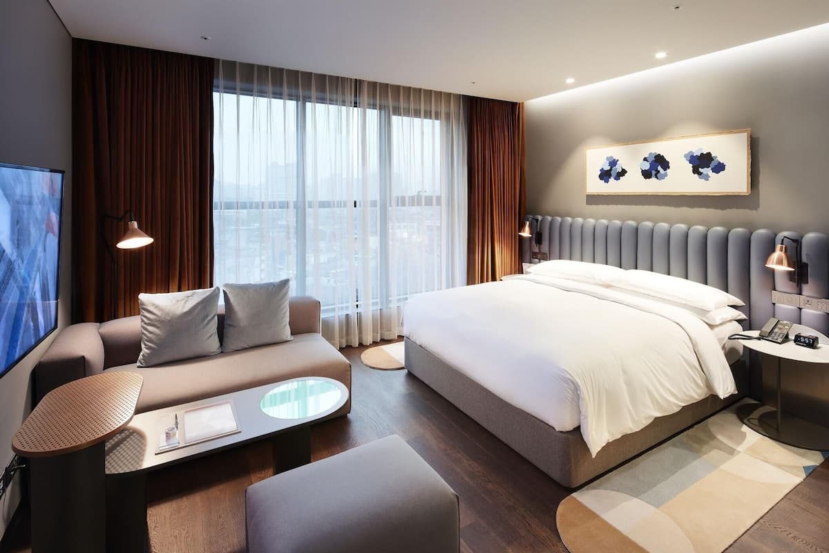 A modern hotel room with a large bed, a sofa, a small table, and a TV.