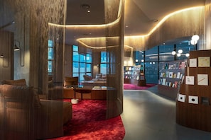 A modern interior with a curved seating area, a red carpet, and a bookshelf with books. - Ryse, Marriot Hotel, Autograph Collection (Seoul)