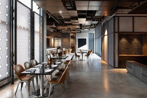 Un comedor moderno con mesas y sillas largas, ventanas amplias y un revestimiento de pared de ladrillo.