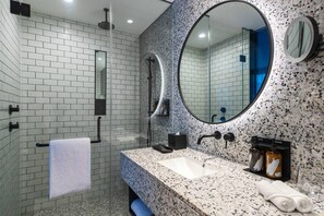 A modern bathroom with a white brick wall, a granite countertop, a large mirror, and a glass shower enclosure. - Ryse, Marriot Hotel, Autograph Collection (Seoul)