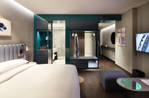 Habitación de hotel moderna con cama, escritorio, zona de ducha y televisión.