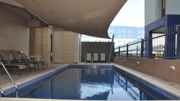 Piscina interior com borda azulejada, escada de metal e algumas cadeiras de descanso.