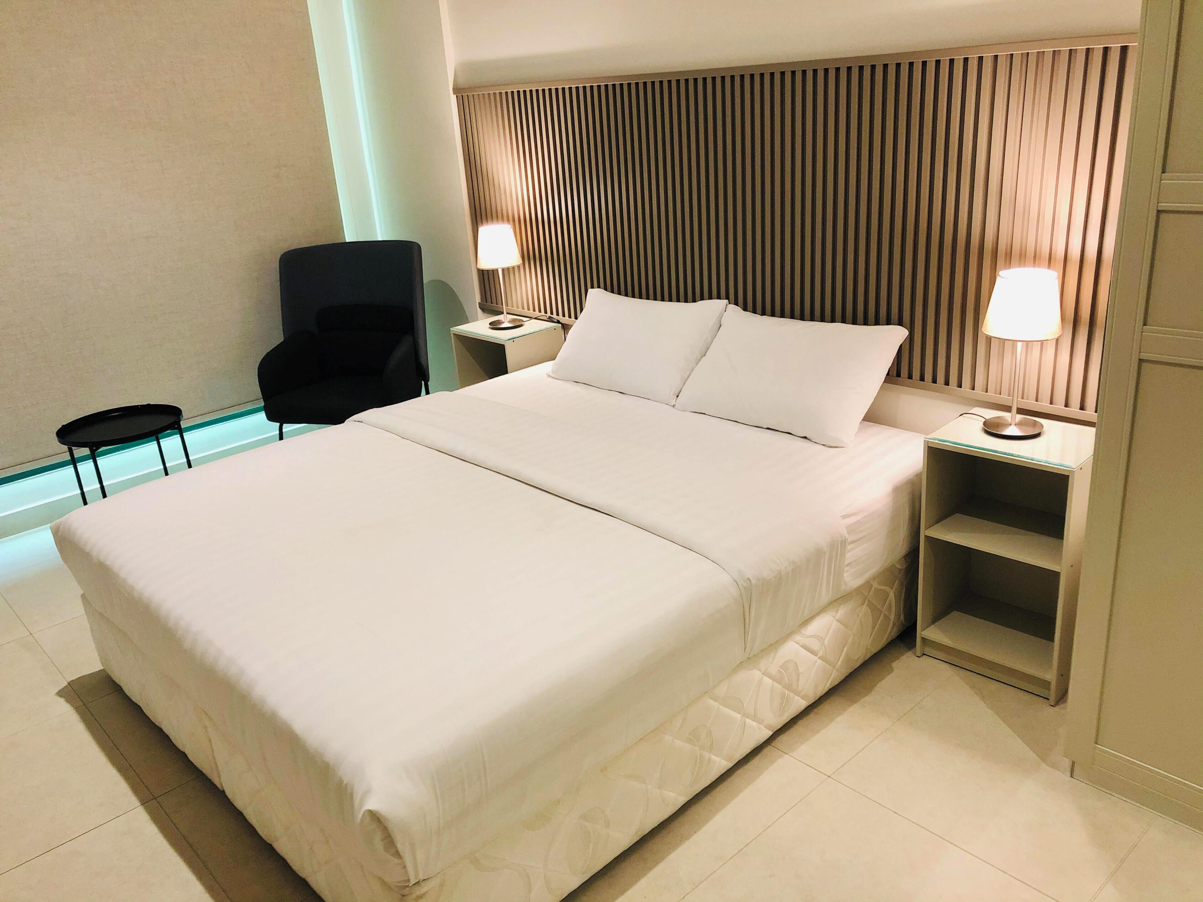 A hotel room with a large bed, two bedside tables with lamps, a chair, and a small table.