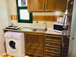 A compact kitchen with a washing machine, a microwave, and a sink. - Times Square Suites (Hawally)