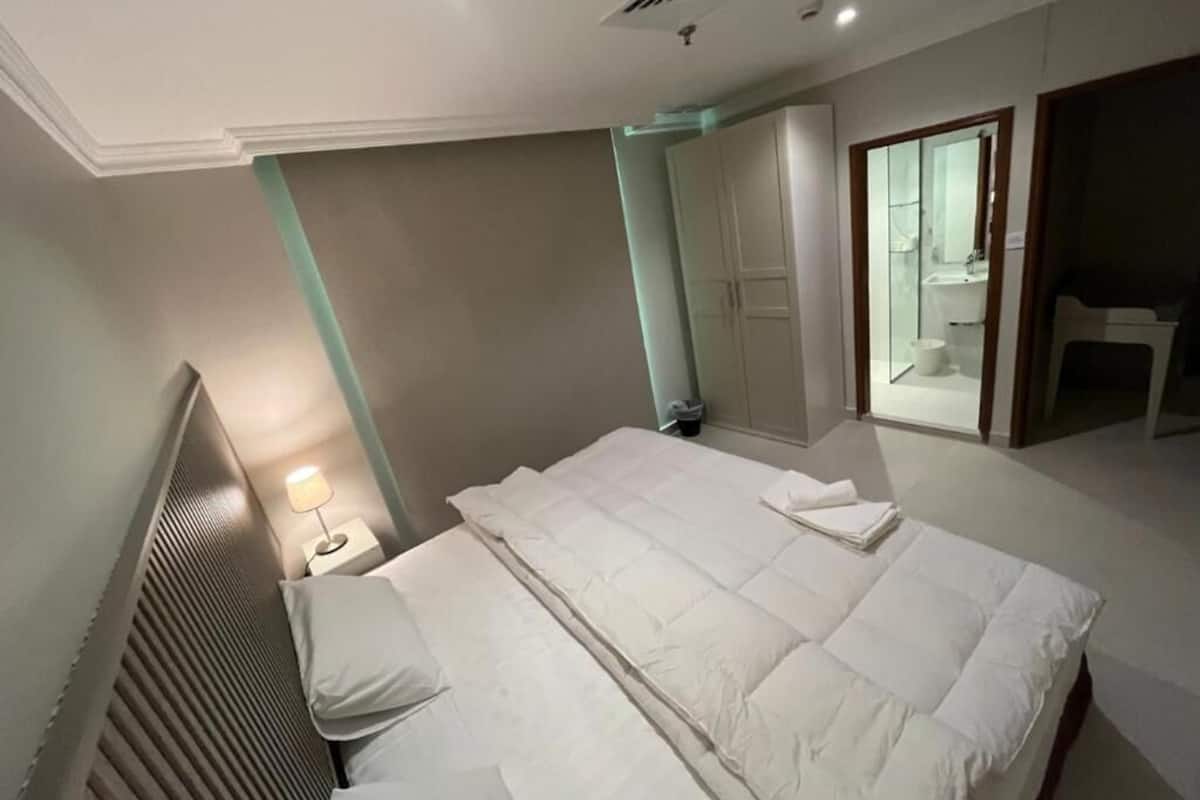 A hotel room with a bed, a nightstand, a lamp, a wardrobe, and a bathroom visible through an open door.