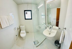 A modern bathroom with a glass-enclosed shower, a toilet, a sink, and a mirror. - Times Square Suites (Hawally)
