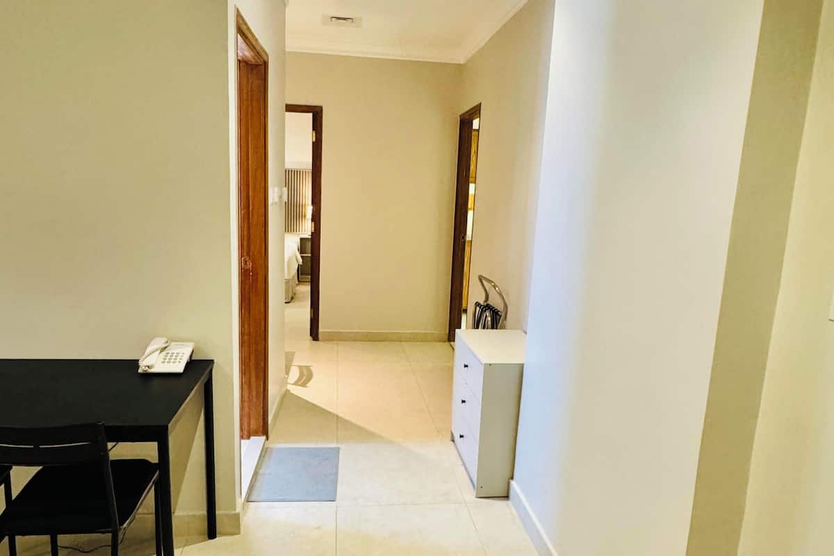 A hallway leading to a bedroom with a bed, a small table with a telephone, and a cabinet.