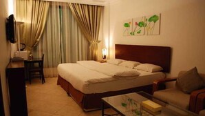 Quarto de hotel com uma cama grande, uma mesa de cabeceira, uma cadeira, uma escrivaninha e uma luminária.