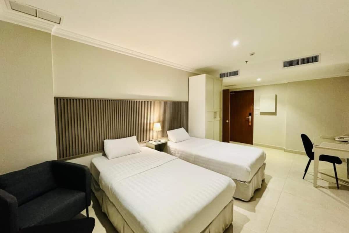 A hotel room with two beds, a desk, a chair, a lamp, and a wardrobe.