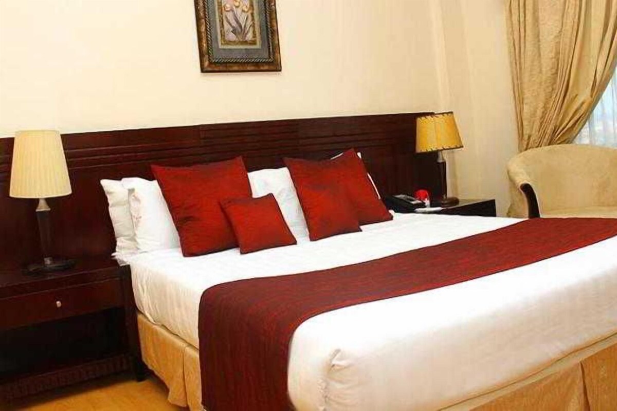 A neatly made bed with red and white bedding, a wooden headboard, and a nightstand with a lamp.