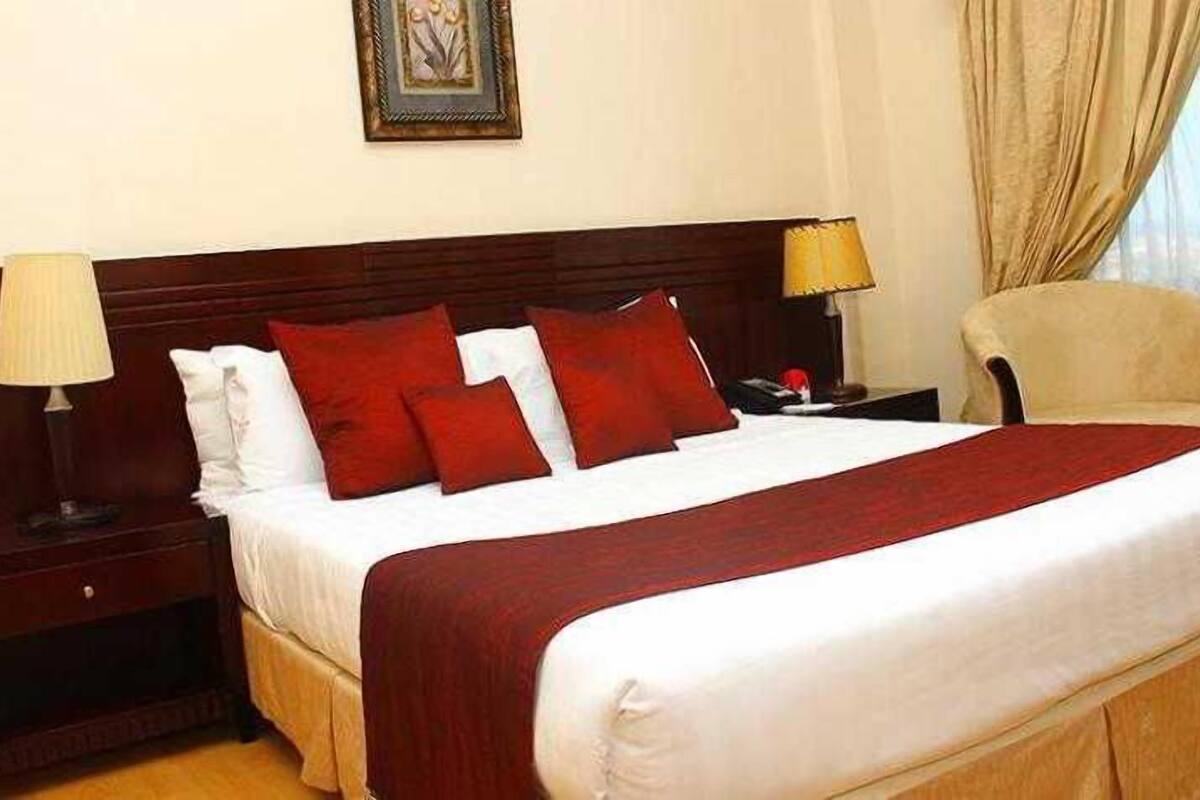 Una cama bien tendida con ropa de cama roja y blanca, un cabecero de madera y una mesita de noche con una lámpara.