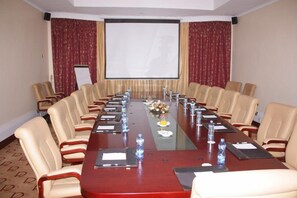 A conference room with a long table, beige chairs, water bottles, and a projector screen. - Boma Inn (Nairobi)