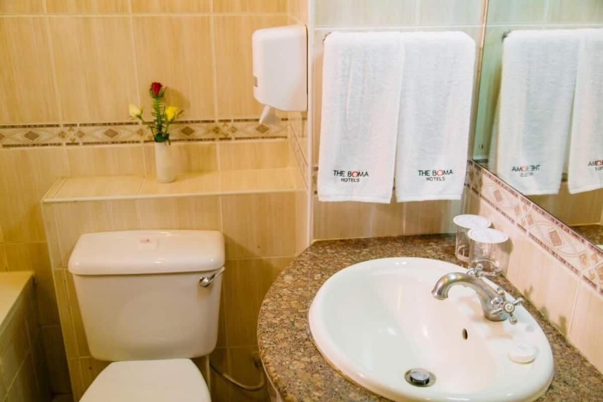 Un baño con inodoro, lavamanos y espejo, con toallas colgadas en la pared.