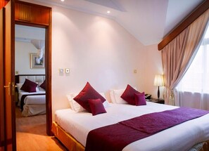 A hotel room with a large bed, two pillows, a bedside table with a lamp, and a window with curtains. - Boma Inn (Nairobi)