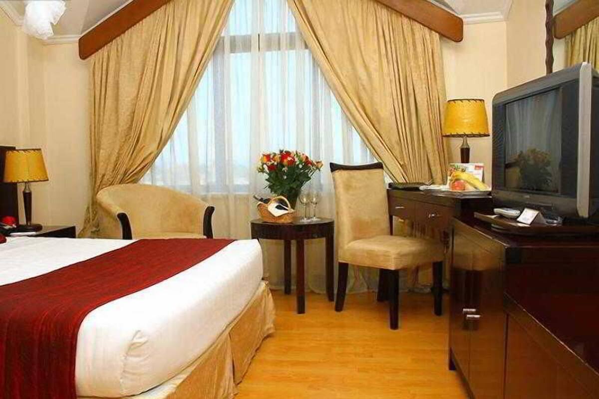 Habitación de hotel con cama, escritorio con televisor, silla y pequeña mesa con un jarrón de flores.