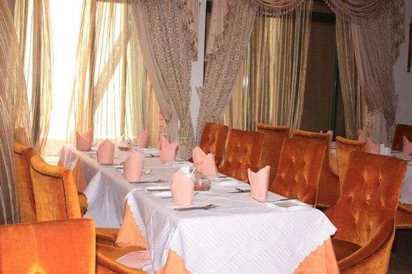 A formal dining room with a long table set for multiple guests, surrounded by upholstered chairs.