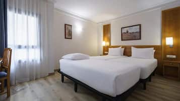 Habitación de hotel con dos camas, una silla de madera y un cuadro en la pared.