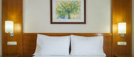 A hotel room with a large bed, two bedside lamps, and a framed artwork on the wall.