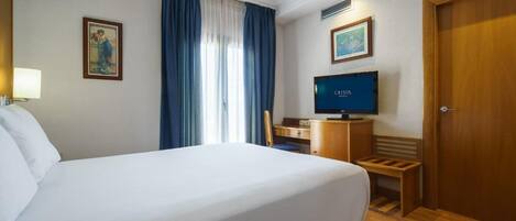Ett hotellrum med en stor säng, ett skrivbord med en dator, en stol och en dörr.