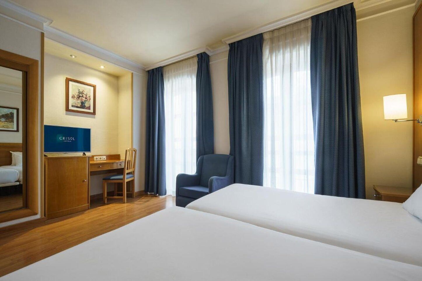 A hotel room with a bed, a desk, a chair, and a TV.