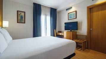 A hotel room with a bed, a desk with a computer, a television, and a door.