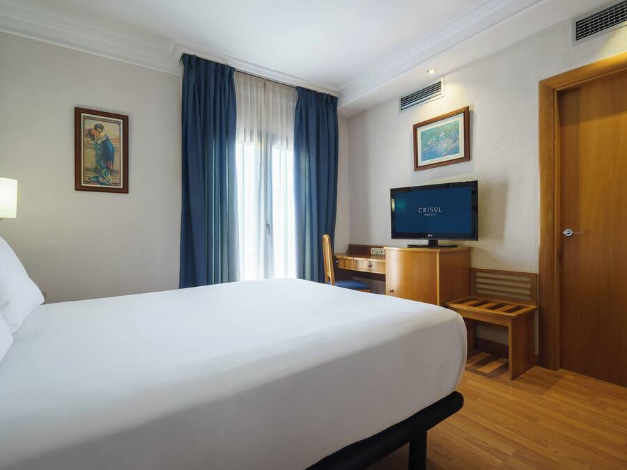 A hotel room with a bed, a desk with a computer, a television, and a door.