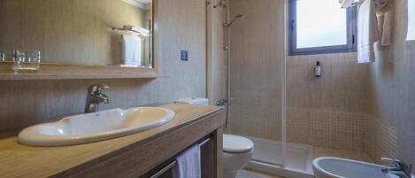 Un baño con tocador de madera, lavamanos, inodoro, ducha y bidé.
