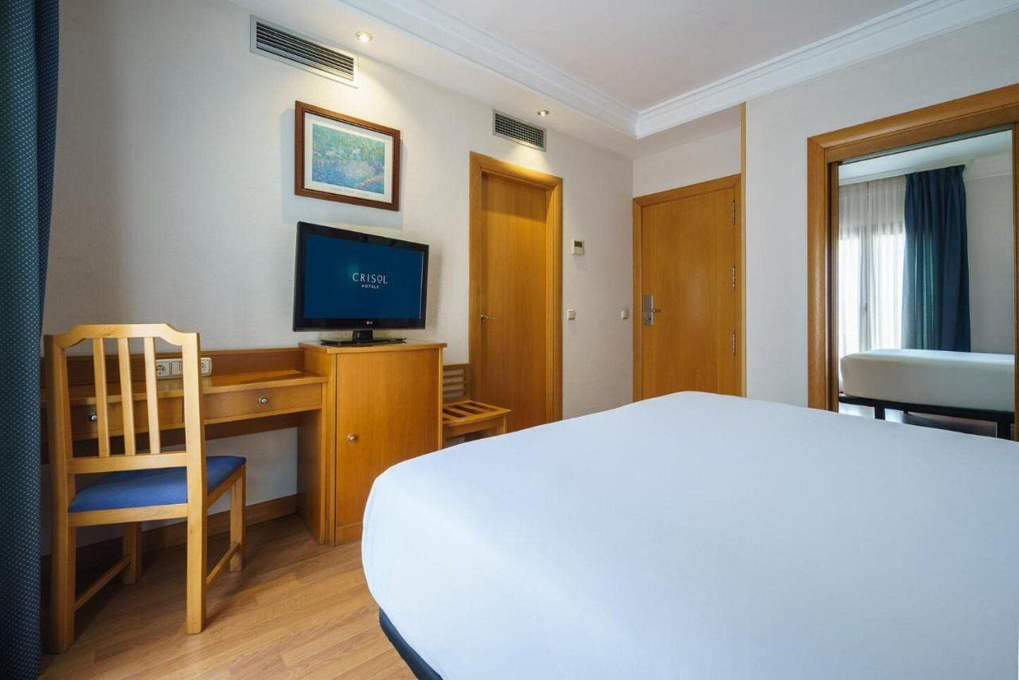 A hotel room with a bed, a desk with a chair, a television, and two doors.