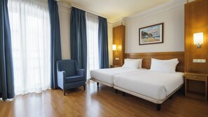 Habitación de hotel con dos camas, una silla, suelo de madera y un cuadro en la pared.