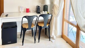 Une chambre d’hôtel équipée d’un téléviseur à écran plat fixé au mur, d’un bureau avec une lampe, de deux chaises, d’une machine à café et d’une poubelle.