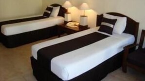 Una habitación de hotel con dos camas individuales, una mesita de noche con lámpara y una silla.