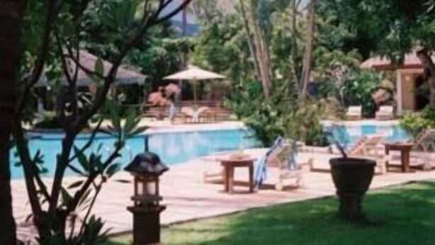 Zona de piscina con sillones de descanso y sombrillas, rodeada de vegetación.