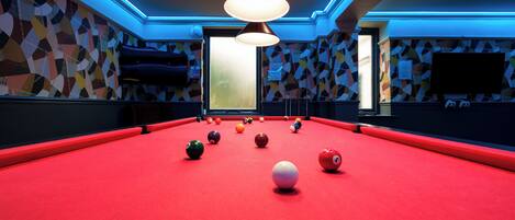 A pool table with balls, a television, and a patterned wall.