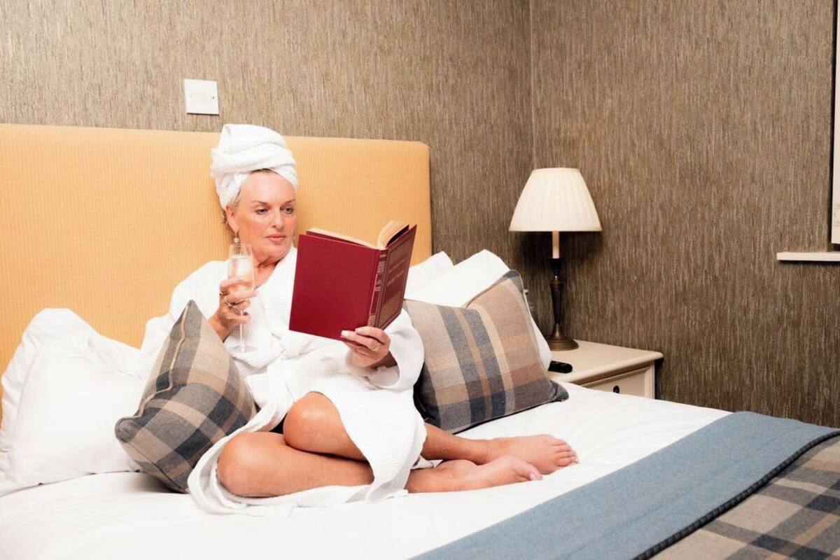Eine Person sitzt in einem Hotelzimmer auf einem Bett und liest ein Buch.