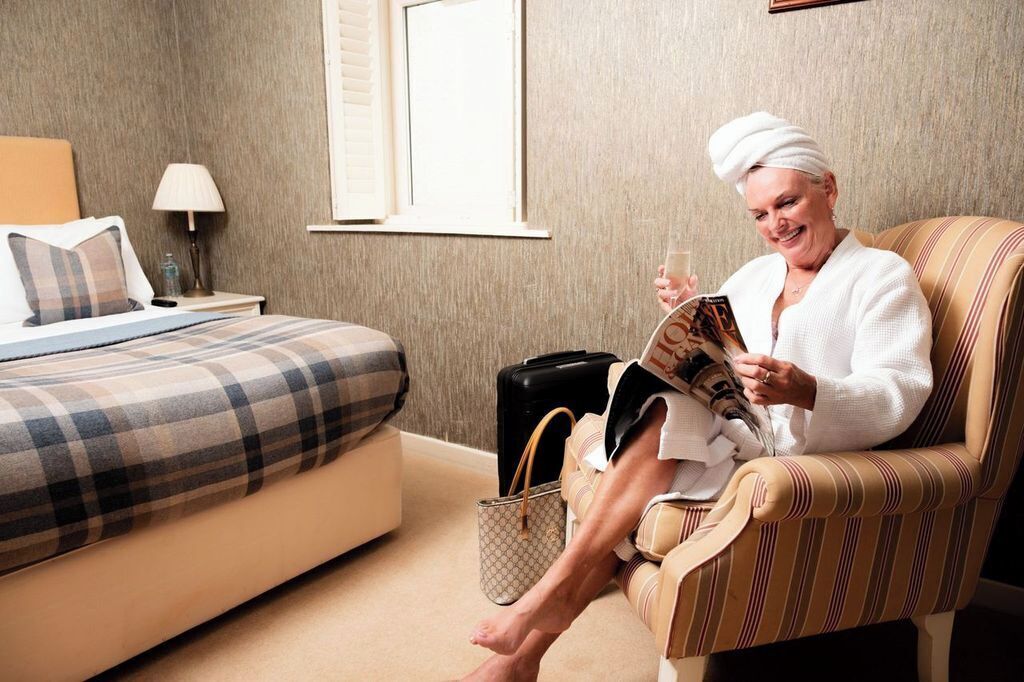 A hotel room with a bed, a chair, a lamp, and a suitcase.