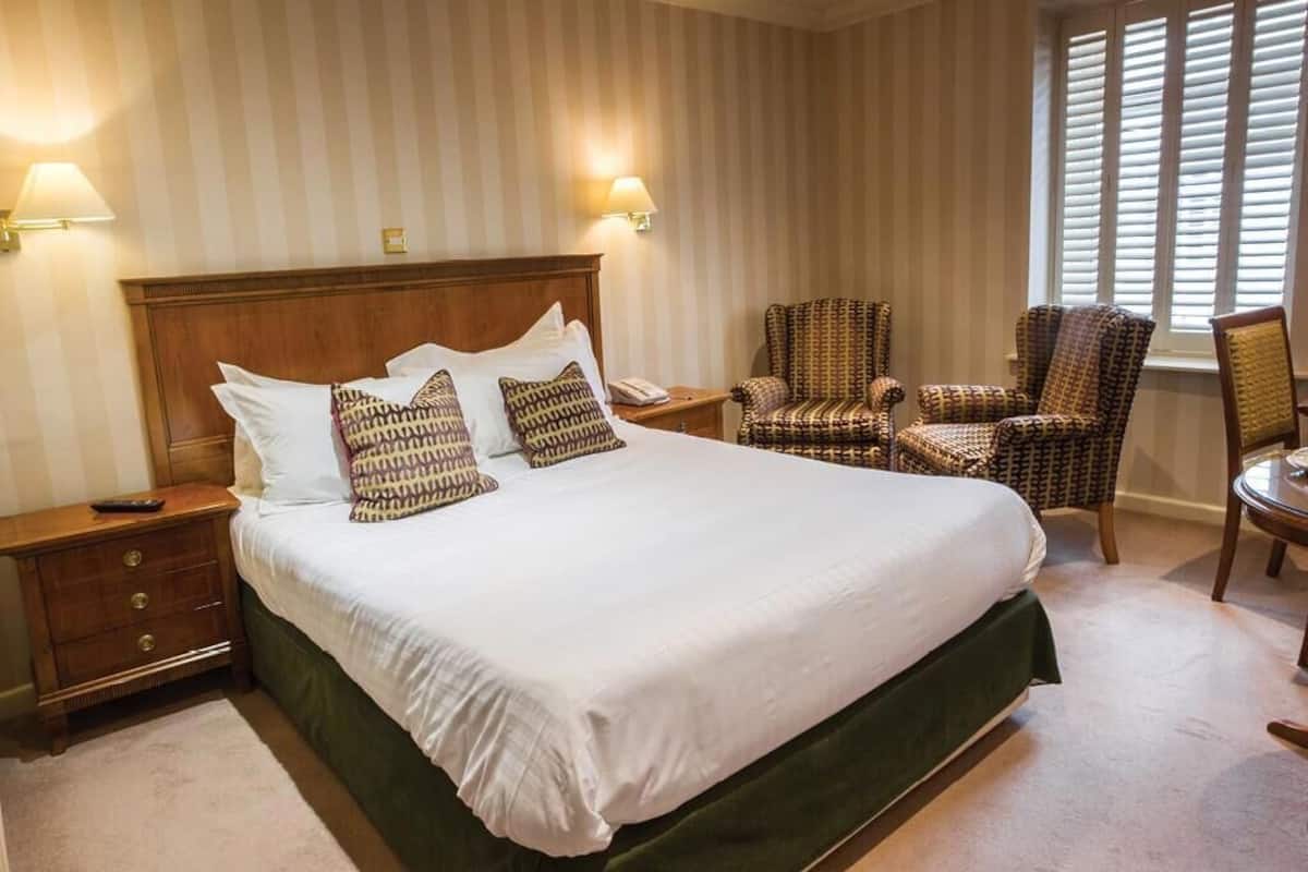 Ein Hotelzimmer mit einem großen Bett, zwei Nachttischlampen, einem Sessel und einem kleinen Tisch.
