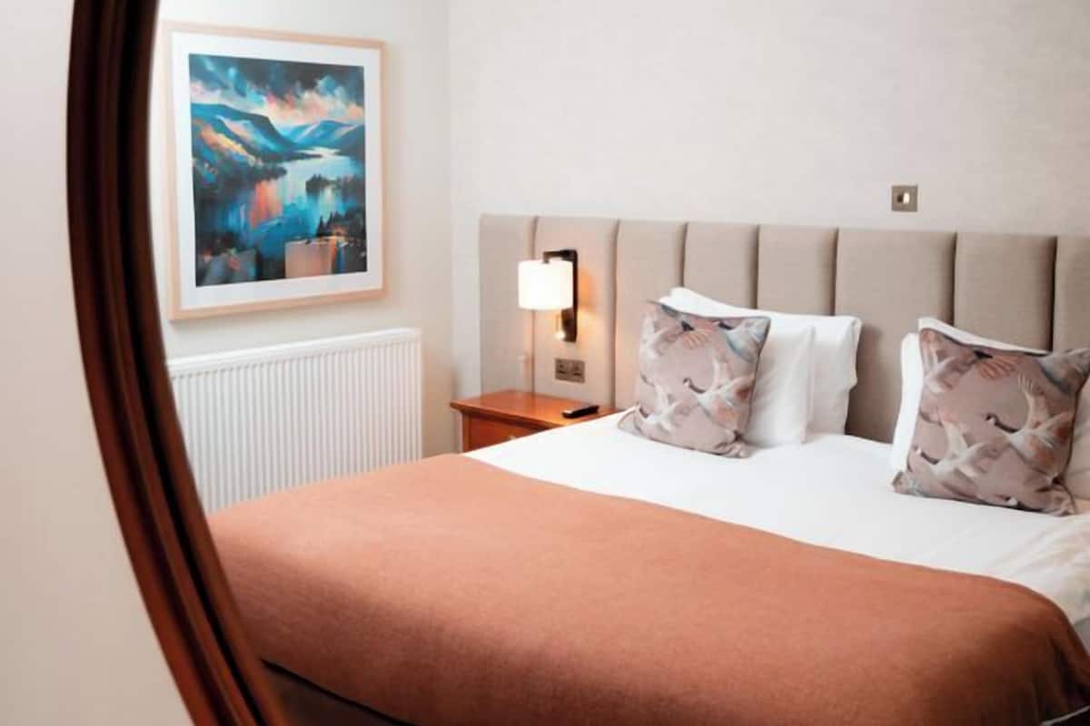 Ein Hotelzimmer mit einem Bett, einem Nachttisch, einer Lampe und einem Bild an der Wand.