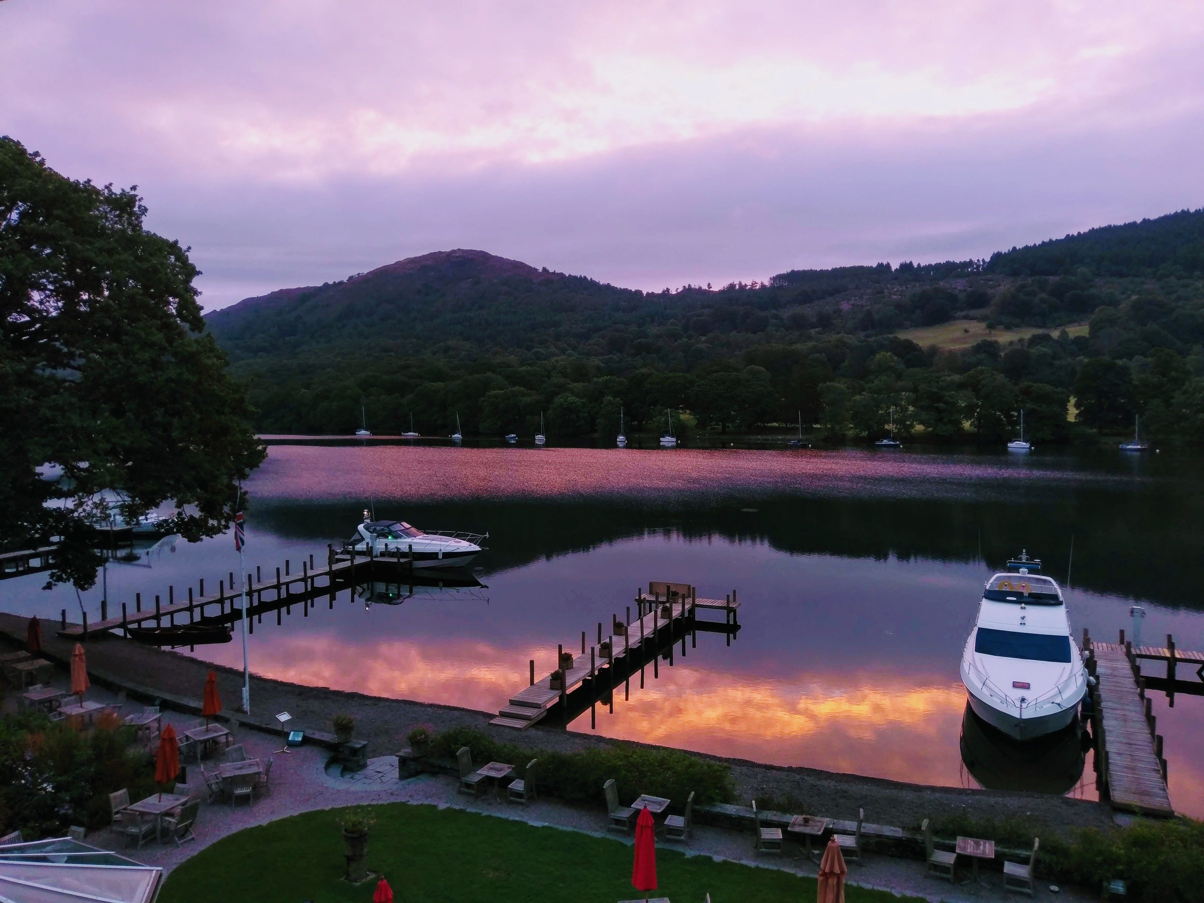 Une jetée au bord du lac avec des bateaux, une plateforme en bois et des sièges en plein air.