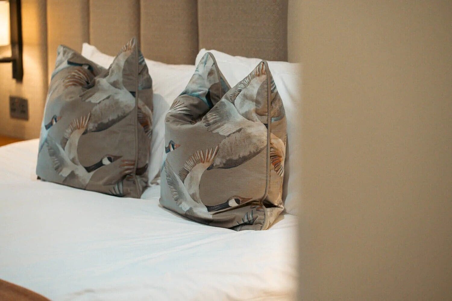 A bed with white linens and two pillows featuring a bird pattern.