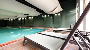 An indoor swimming pool with tiled flooring, lounge chairs, and a green wall.