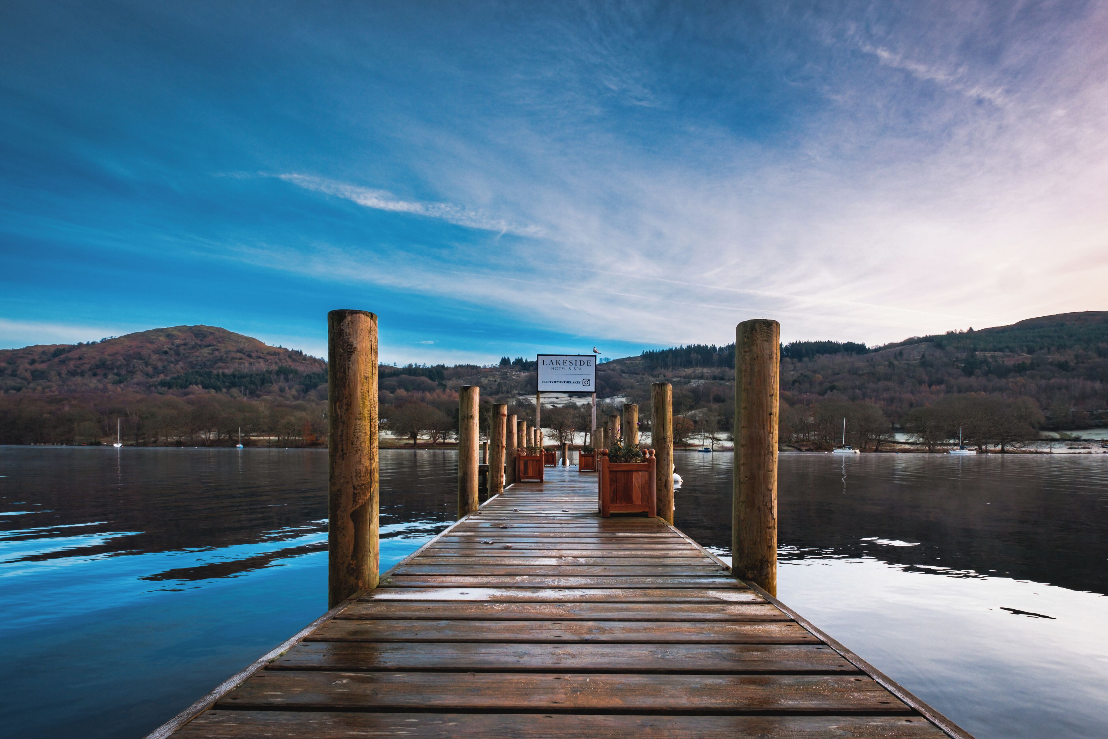 A wooden pier extending into a calm lake with a sign reading "LAKESIDF" and a view of hills in the distance.