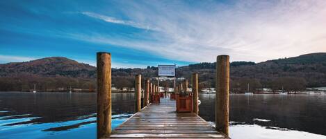 A wooden pier extending into a calm lake with a sign reading "LAKESIDF" and a view of hills in the distance.